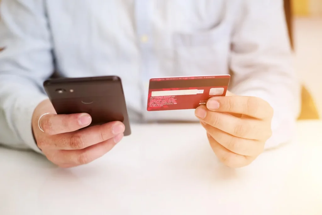 A person holding a credit card next to a smartphone displaying a shopping app, illustrating how to earn cashback and rewards while shopping online.