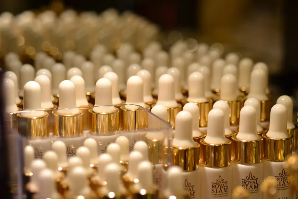 Rows of white skincare serum bottles with gold dropper caps, highlighting luxury cosmetic packaging.